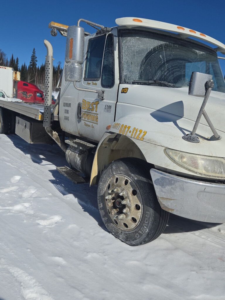 Front-side view of a snowy Best Towing flatbed truck parked in winter conditions.