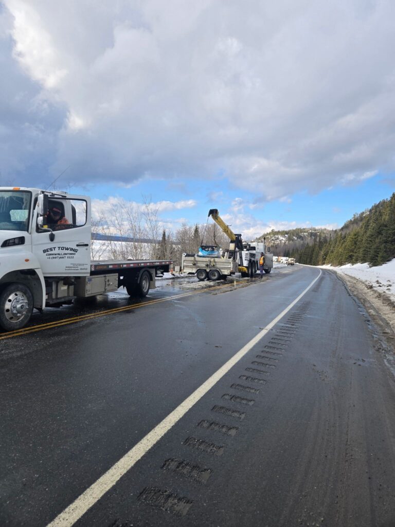 Best Towing flatbed truck and recovery crew assisting a vehicle on a snowy highway in Ontario.